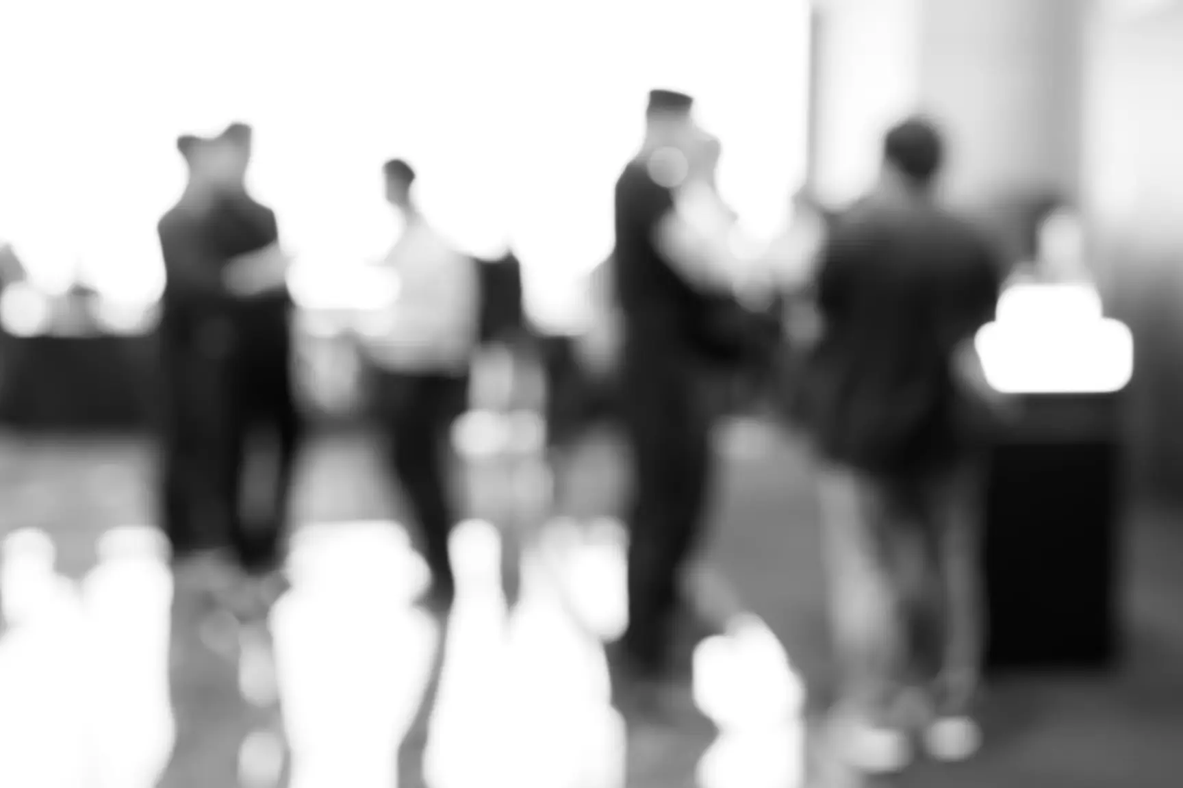 Blurred image of people standing and talking at an event indoors.