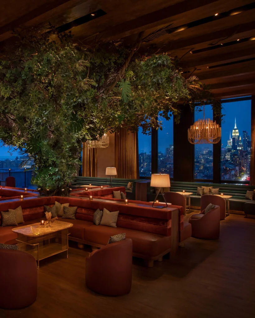 A cozy upscale lounge with lush greenery and city skyline views.