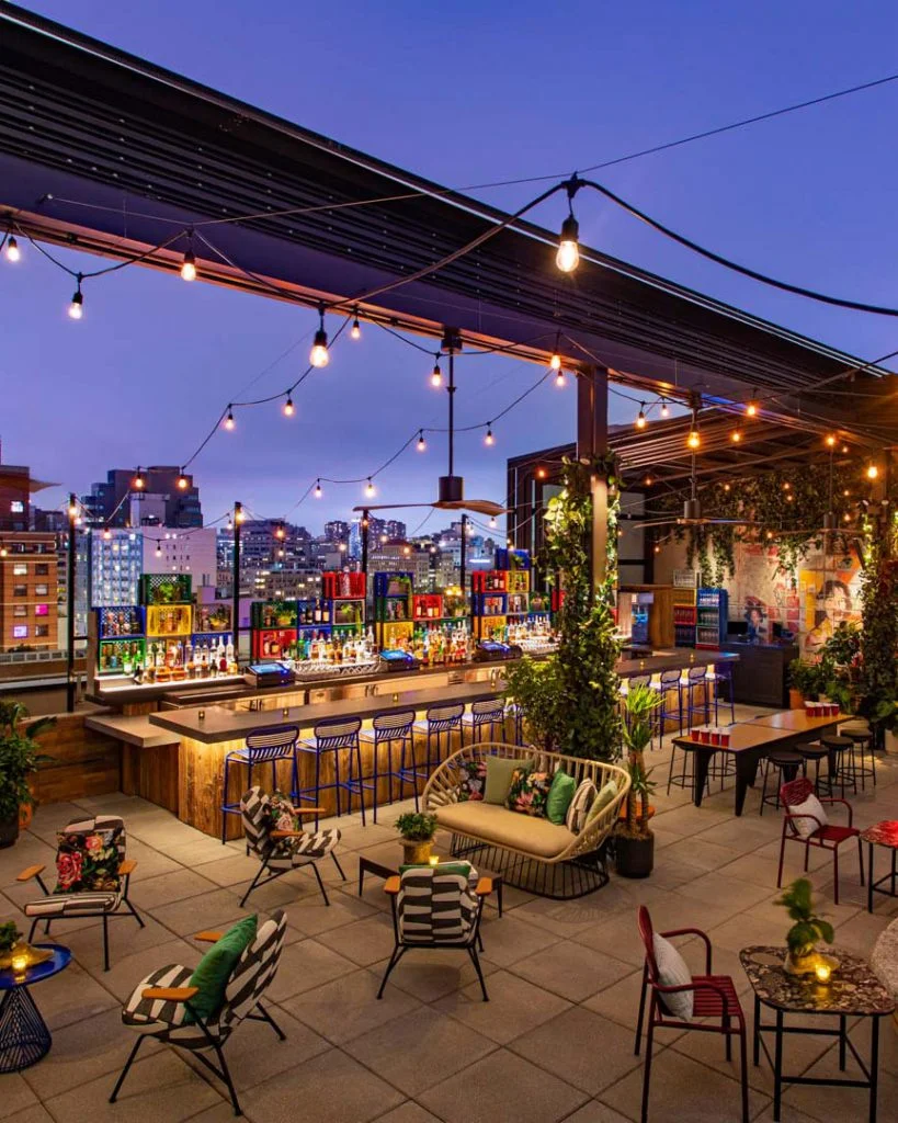 Rooftop bar with colorful seating, string lights, and city views.